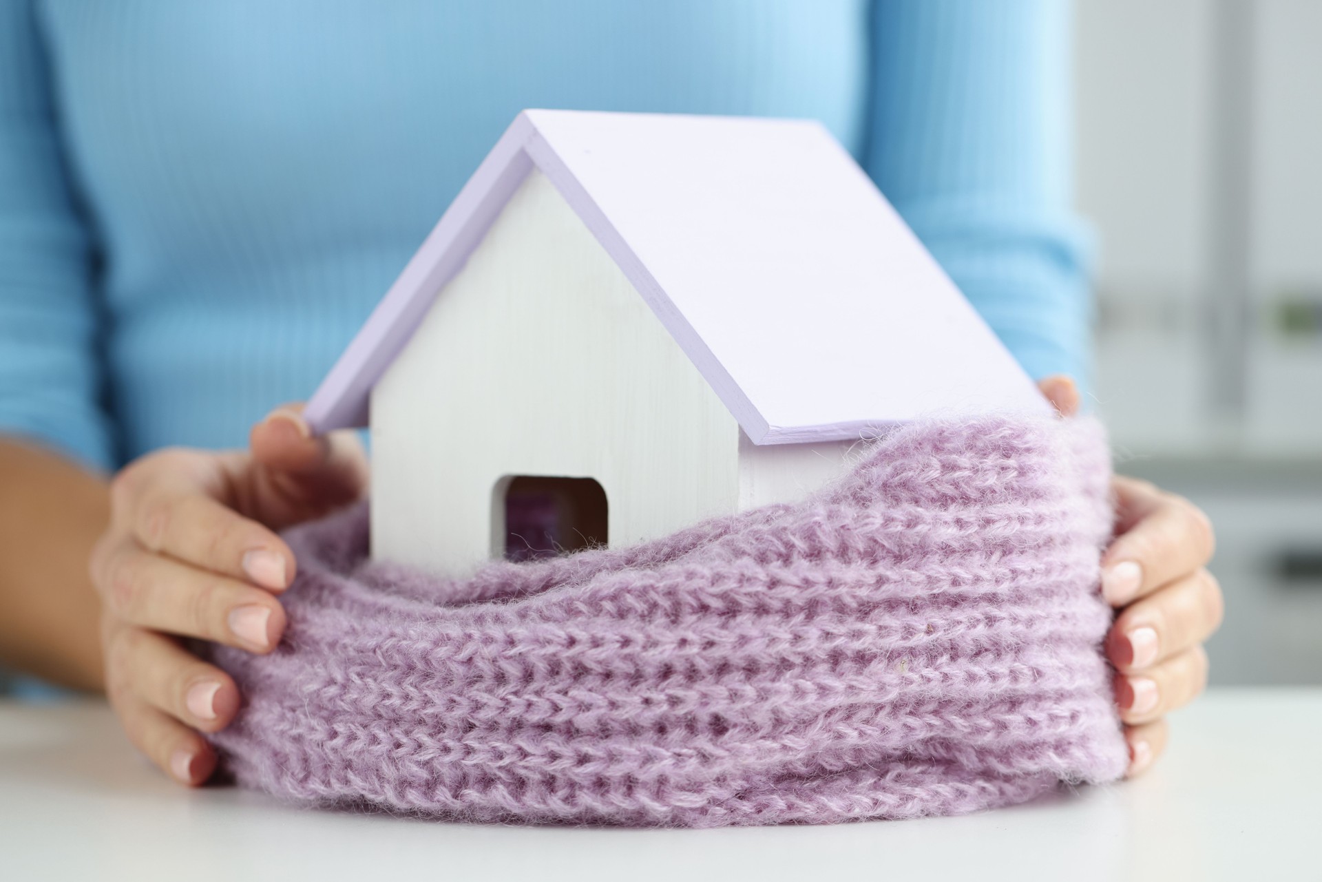 Woman wrapped small wooden house in warm scarf